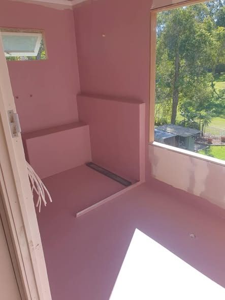 Pink waterproof membrane applied across a Brisbane wet-area with a bench seat and window view
