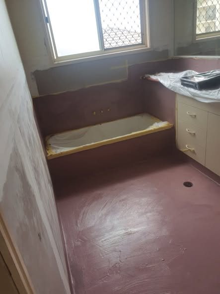 First coat of pink membrane across walls and bench in a bathroom